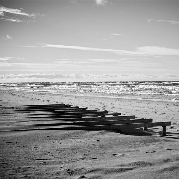 A black and white photo depicting a peaceful beach with wooden benches